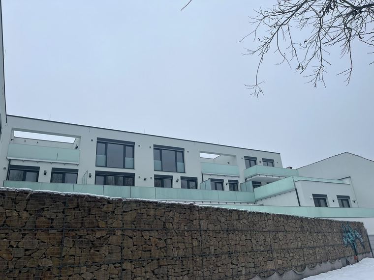 Bytové domy s dokončenými fasádami a kamennou opěrnou zdí