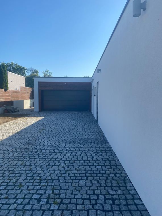 Novostavba s bílou fasádou a dlážděným vjezdem